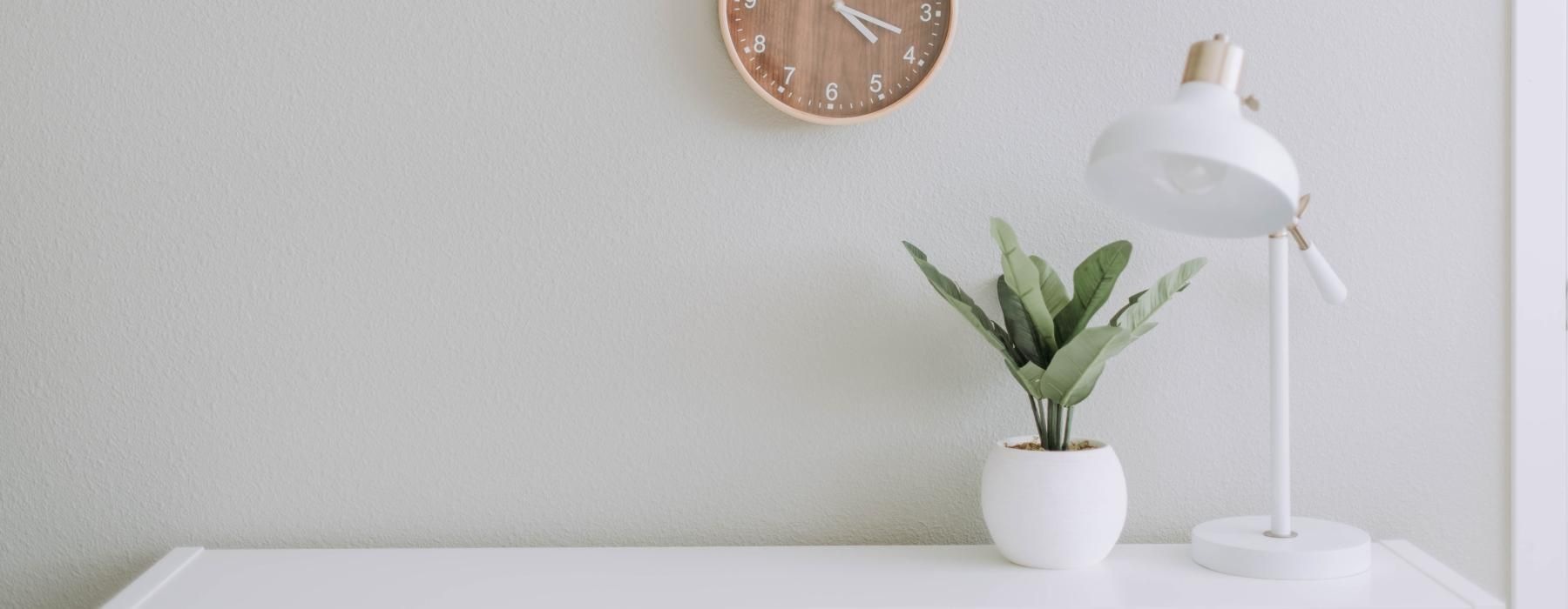 clock on a wall over a desk with a lamp and potted plant